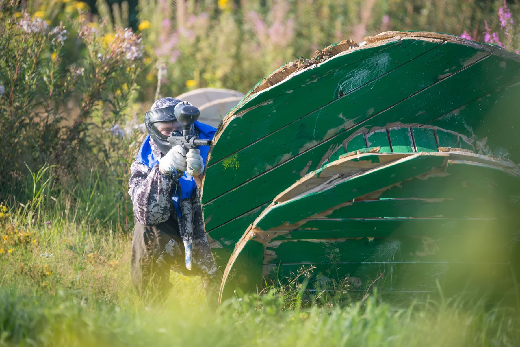 Paintball sport player in protective uniform and mask playing with gun outdoors and hiding.
