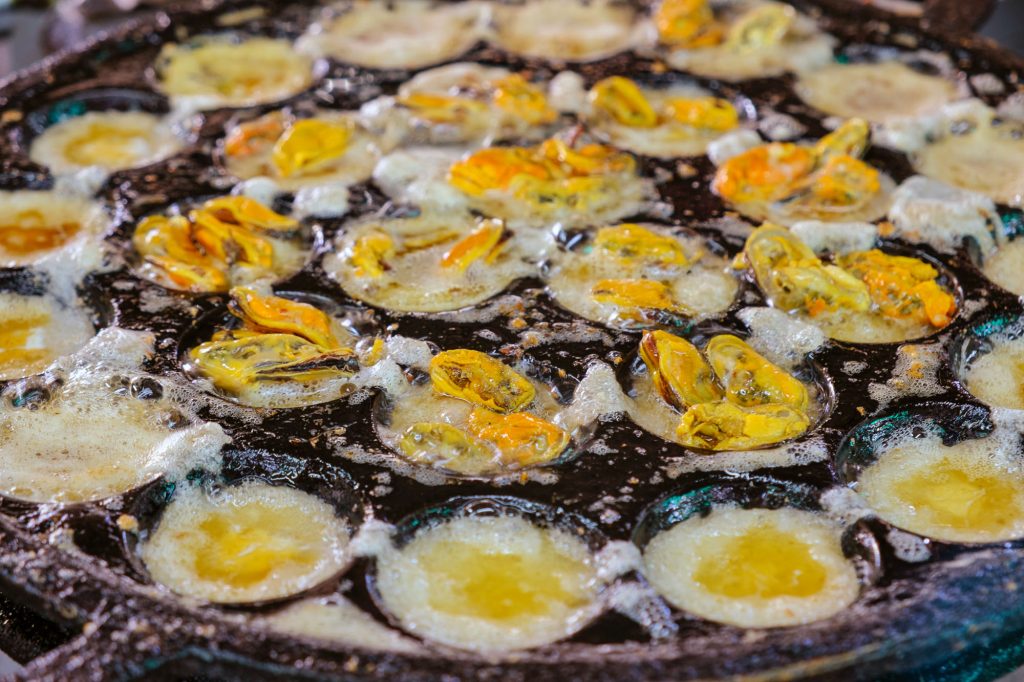 Fried egg with mฟussels boiling in Kanom Krok iron pan. Thai seaf